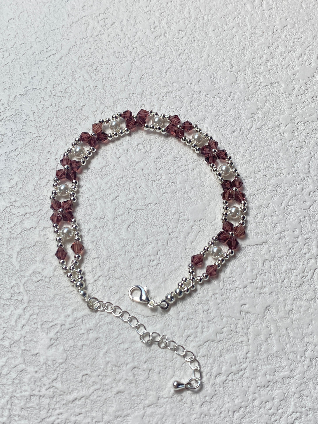 A handmade bracelet featuring plum-colored seed beads and silver accents, arranged in an elegant pattern with an adjustable chain clasp for a perfect fit.