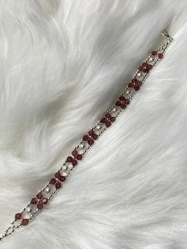 A handmade bracelet featuring plum-colored seed beads and silver accents, arranged in an elegant pattern with an adjustable chain clasp for a perfect fit.