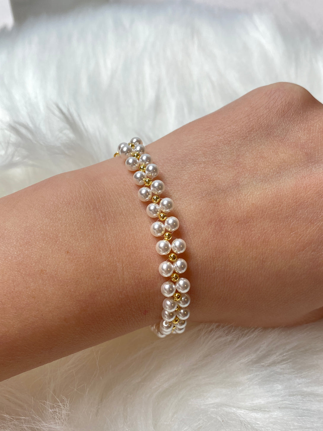 A handmade bracelet featuring pearl-style glass beads and gold accents, designed with an adjustable chain for a comfortable and elegant fit.