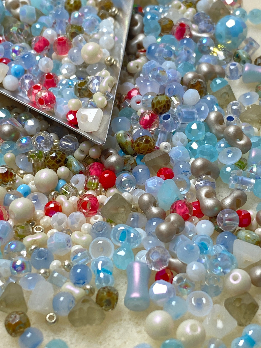 A vibrant mix of ocean-toned seed beads featuring shades of blue, white, pearl, red, and green, displayed with a metal scoop. Ideal for DIY jewelry projects, the kit includes memory wire and smooth needle-nose pliers for easy crafting.