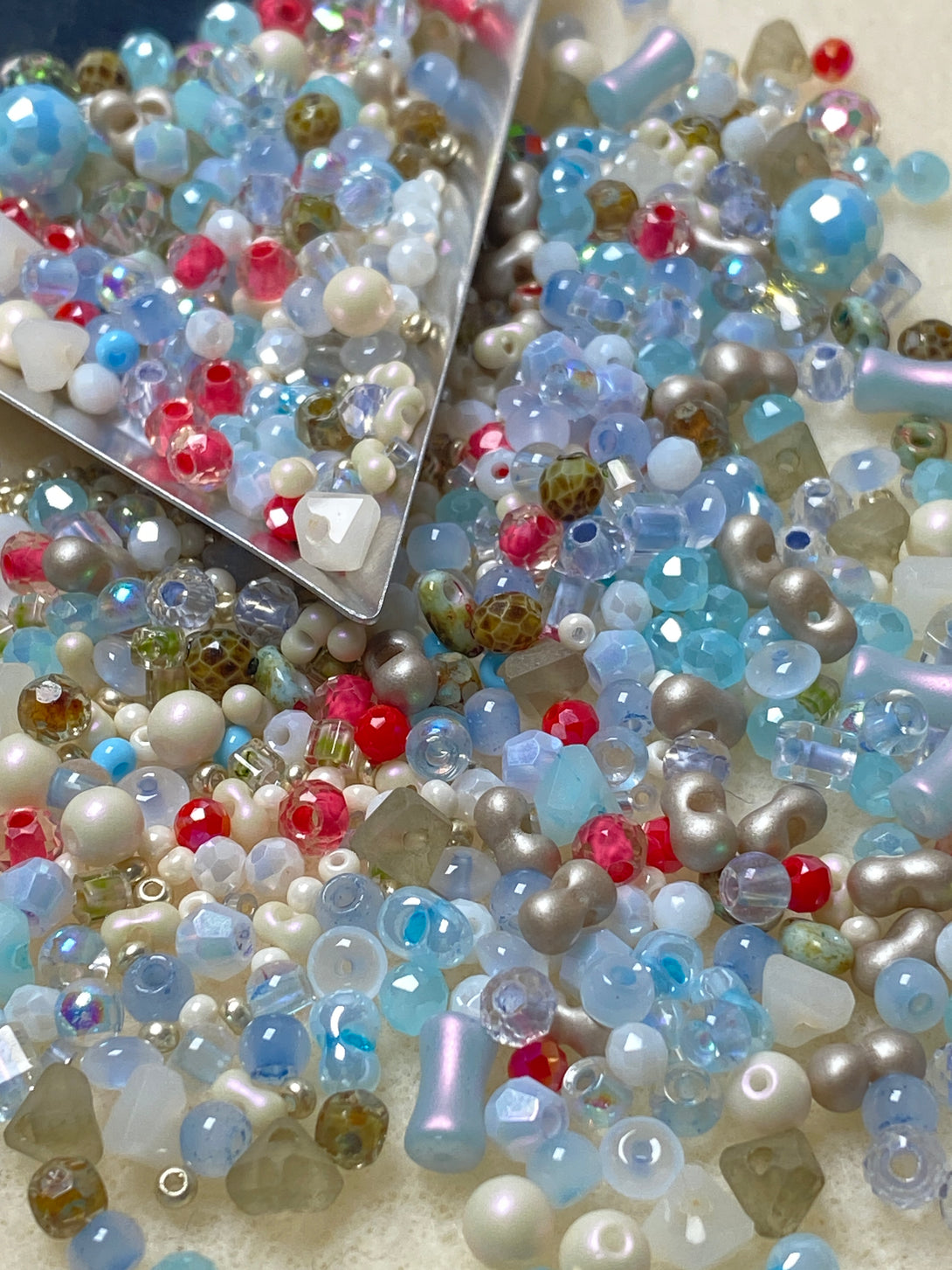 A vibrant mix of ocean-toned seed beads featuring shades of blue, white, pearl, red, and green, displayed with a metal scoop. Ideal for DIY jewelry projects, the kit includes memory wire and smooth needle-nose pliers for easy crafting.